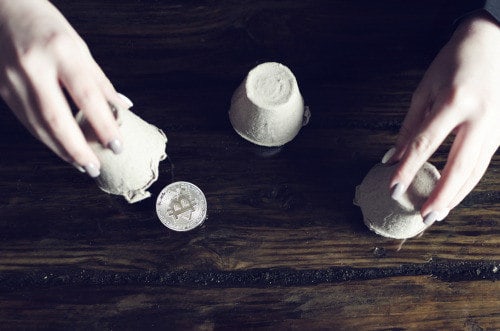 Close-up of hands playing a shell game with a bitcoin coin. Buy bitcoin easily on Coinmama.